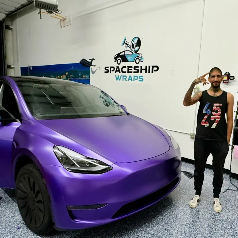 Raoul Shah standing beside a purple-wrapped Tesla in his vehicle wrap shop